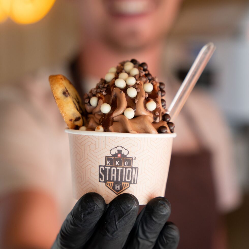 Coupe glacée au chocolat KKO Station tendue par une main gantée
