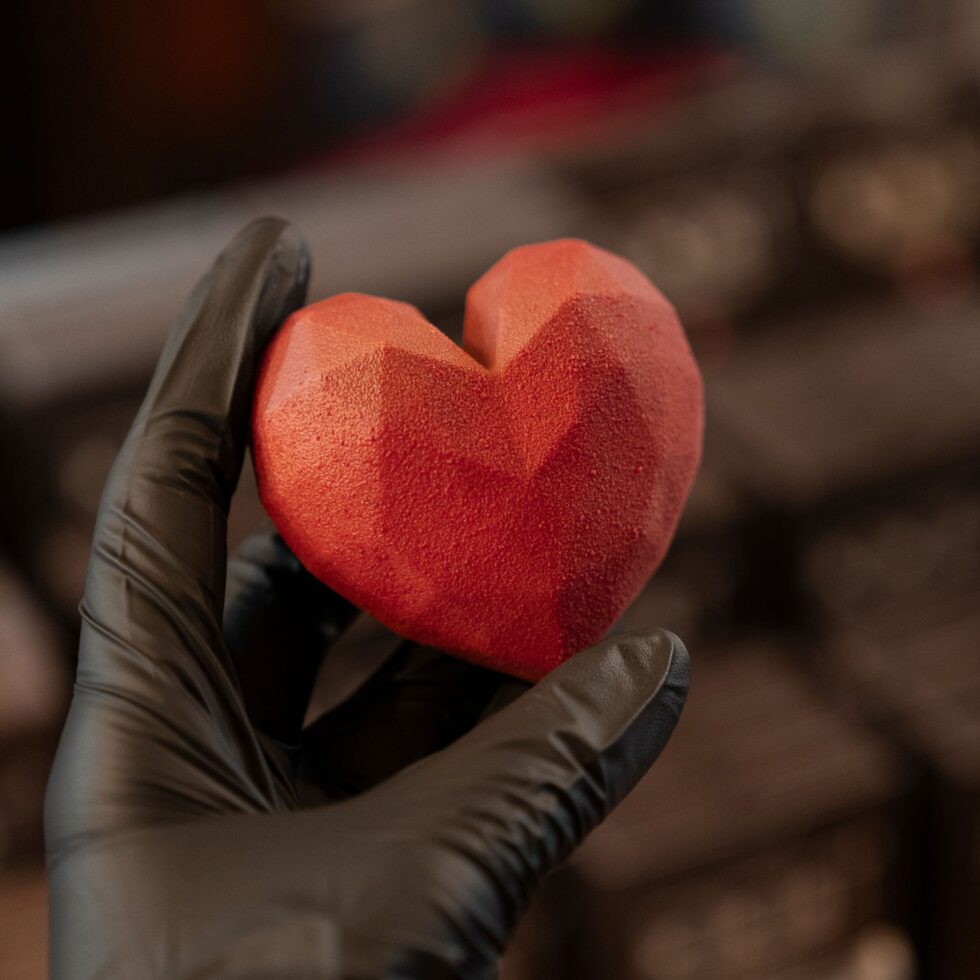 Cœur en chocolat rouge tenu dans une main gantée